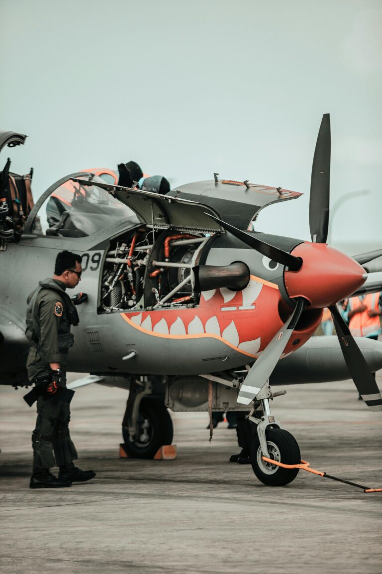A pilot inspects a military aircraft with an open engine on the tarmac.